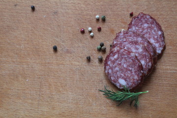 on a wooden board lies several slices of smoked sausage with peppercorns and dill seasoning with a place to insert text or product goods