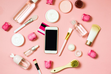 Obraz na płótnie Canvas Concept of online shopping cosmetics. Top view on cosmetics bottles, cream, soap, makeup brushes, mobile phone on a pink background, flat lay,