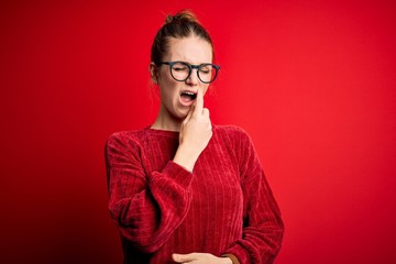 Young beautiful redhead woman wearing casual sweater over isolated red background bored yawning tired covering mouth with hand. Restless and sleepiness.