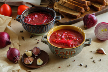 Soup borscht on a beige background in a clay plate with garlic, onion, pepper, sour cream and bread