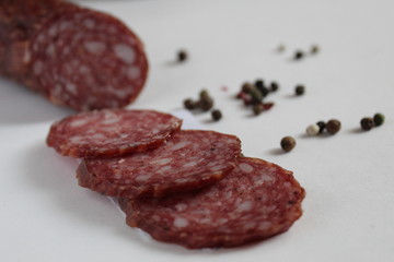 a stick and sliced pieces of smoked sausage lies on a white background next to the pepper peas black white red in the background pepper and baguette
