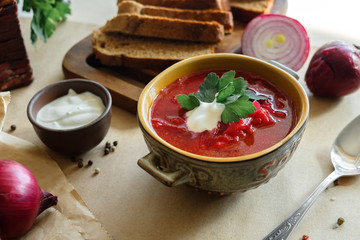 Soup borscht on a beige background in a clay plate with garlic, onion, pepper, sour cream and bread