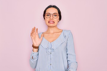 Young beautiful woman wearing casual striped shirt and glasses over pink background disgusted...