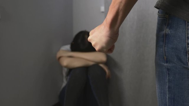 An aggressive male partner bullies his wife. The poor girl covers her face with her hands.
