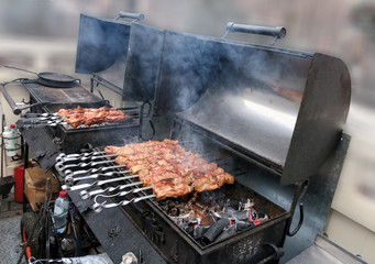 Meat with smoke on a barbecue grill over charcoal. Grilled cubes of meat on metal skewer. Meat on skewers is roasted on fire.