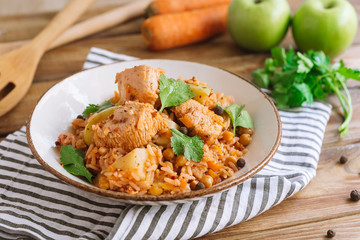 Deep plate with hot turkey pilaf with chickpeas, allspice, carrots, parsley leaves on top. On a...