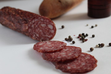a stick and sliced pieces of smoked sausage lies on a white background next to the pepper peas black white red in the background pepper and baguette