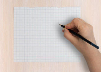 Female hand is going to write with a pencil on an empty notebook sheet
