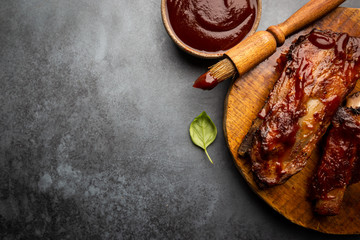Delicious BBQ baby-back ribs with tangy sauce and a basting brush on black background, top view