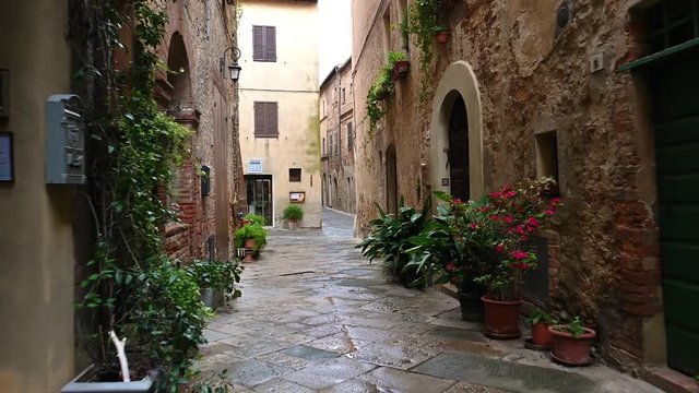 Smooth camera steady slide shot around old Tuscany village Pienza narrow empty streets, with old stone walls, shelled facades with flowers, early in the morning