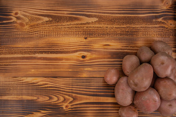 Heap of raw red potatoes on wooden textured background. Fresh vegetables, top view with copy space