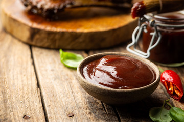 Barbecue sauce in a saucer with basting brush over rustic barn wood table with copy space.