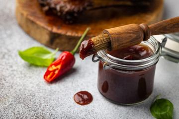 Barbecue sauce in glass jar with basting brush over gray stone table with copy space.