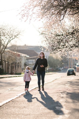 Fototapeta premium Coronavirus and Air pollution concept. Little girl and mother wearing masks walk on street. Pandemic virus symptoms. Family with kid outdoors against the background of tree blossom. Illness protection