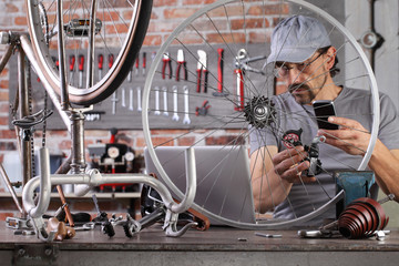 man repair the vintage bicycle with mobile phone at the computer search spare parts on the internet...