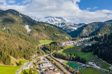 Fototapeta na wymiar Aerial view of improbable green meadows of Italian Alps, Comano Terme, huge clouds over a valley, roof tops of houses, Dolomites on background, sunshines through clouds
