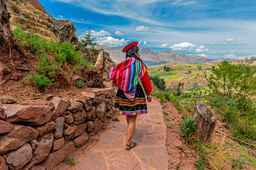 Quechua Indigenous Woman in traditional clothes walking along ancient Inca Wall in the ruin of Tipon, Cusco, Peru. - obrazy, fototapety, plakaty