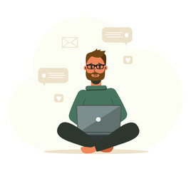 A bearded young man works at a laptop computer. Sits in a lotus position.