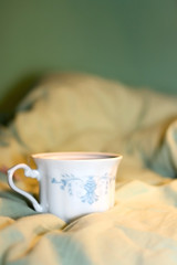 Tea in a vintage porcelain cup on a bed. Selective focus.