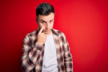 Young handsome caucasian man wearing casual modern shirt over red isolated background Pointing to the eye watching you gesture, suspicious expression