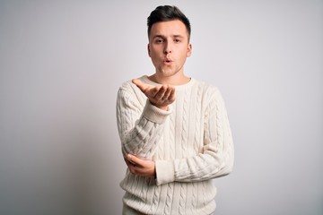 Young handsome caucasian man wearing casual winter sweater over white isolated background looking at the camera blowing a kiss with hand on air being lovely and sexy. Love expression.
