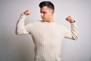 Young handsome caucasian man wearing casual winter sweater over white isolated background showing arms muscles smiling proud. Fitness concept.