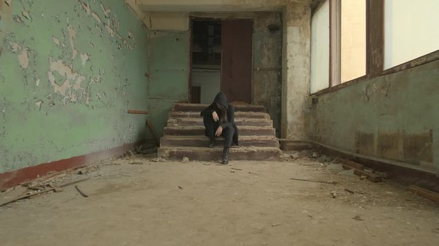 girl in a black hood is sitting in the stairs,the ruined abandoned old wreck corridor,