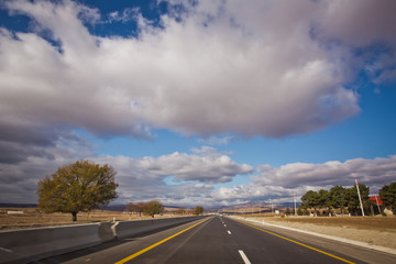 Fototapeta premium Asphalt road and bright blue sky with fluffy clouds . Empty desert asphalt road from low angle with mountains and clouds on background. road, red desert landscape . Open road with blue clouds .