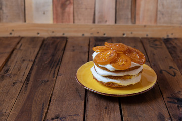 geschichtete Torte mit Quark, Sahne, Rührteig und kandierte Zitronenscheiben auf gelben Teller und braunen Tisch aus Holz