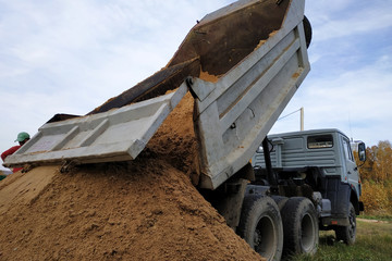 A dump truck unloads sand at a construction site to mix cement.