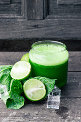 Green apple smoothie in glass and kale leaves on wooden table