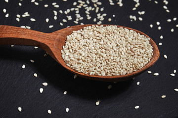 Sesame seeds and a wooden spoon on a dark table. Healthy food and drink concept. Top View.