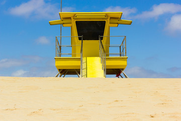 Front side of yellow lifeguard station off duty on empty beach in Corralejo natural park, Fuerteventura. Baywatch tower with blue sky and clouds on background. Emergency profession concept