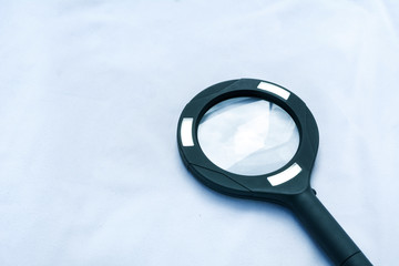 A black magnifying glass isolated on white background, with a blue hue representing science and research.