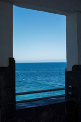 From a concrete and brick window, you can see outside the fresh blue sea illuminated by sunlight.