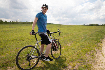 Fototapeta premium Man with bicycle in full cycling equipment in green summer field, active healthy lifestyle in nature envirment