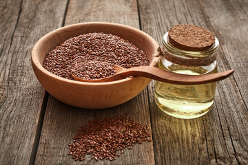 Flax seeds and a wooden spoon on a wooden table. Wooden bowl with bottle of oil. Healthy food and drink concept.