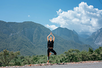 Woman doing yoga poses outside and beautiful view of mountains and sky with clouds