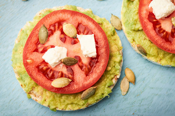 Top view rice cake with avocado and tomato and feta cheese with pumpkin seeds for breakfast