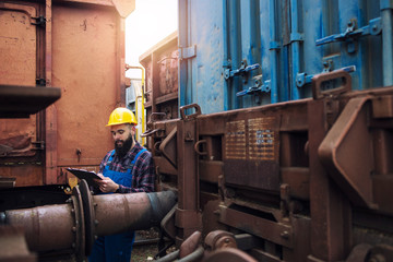Train maintenance railroad worker checking wagons and cars before departure.