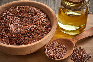 Flax seeds and a wooden spoon on a wooden table. Wooden bowl with bottle of oil on Cutting board. Healthy food concept.