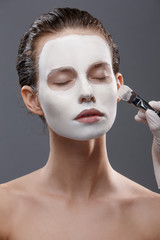 Beautiful girl is applied a white cosmetic mask from black dots. Isolate, studio.