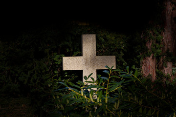 White christian granite cross in a dark mysterious forest with green foliage with copy space. Symbol for christianity, resurrection and Jesus Christ.