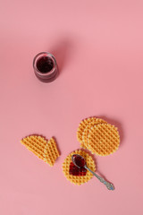 Crunchy cookies, waffles or snacks and a little pot of jam on a solid pink background. Copy space, top view