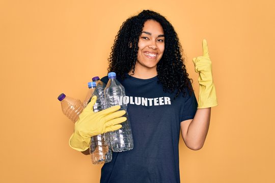 Young african american woman doing volunteering recycling holding plastic bottles surprised with an idea or question pointing finger with happy face, number one