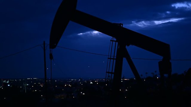 Oil well Pumpjack (Horsehead) pumping at night. Oil pump working after sunset, industry city on the background