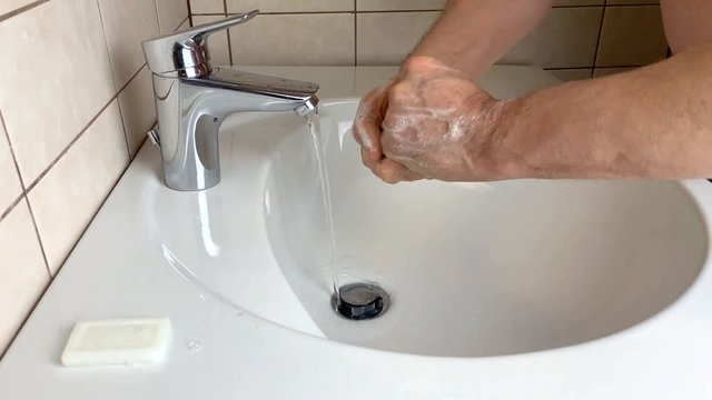 man washes his hands in the bathroom in a white ceramic sink under the tap, the concept of cleanliness and hygienic routine