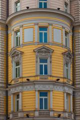 Fragment of the facade of an old building in the shape of a round tower with windows framed by stucco patterns