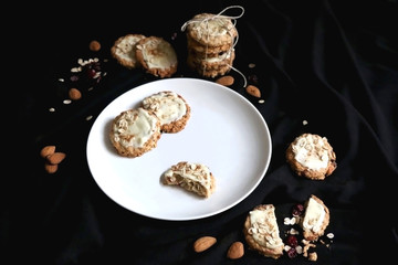 Oatmeal, almond, cranberry and white chocolate cookies on a plate. Selective focus, black background.