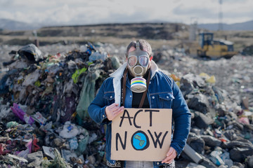 Man with gas mask and placard poster on landfill, environmental concept.